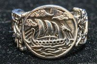 Close-up photo showing the front of the sterling silver ring with a raised depiction of a Viking longship (Drakkar) with sails and serpent head prow, set in a circular medallion.