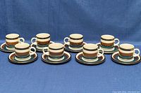 Eight sets of Arabia Kaira mugs and saucers displayed on blue fabric background, showing side and angled views.