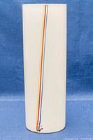 Full view of the white frosted glass cylindrical vase with a single vertical stripe of multiple colors (blue, yellow, orange, red).