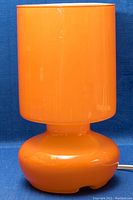 Full frontal view of the retro orange glass table lamp showing its cylindrical shape and smooth finish.