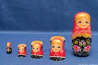 All five Matryoshka dolls displayed standing, showing painted traditional female figure and floral designs in front view.
