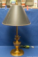 Full view of the brass table lamp showing base, stem with pineapple motif, and black lampshade with pineapple finial on top.