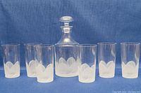 Full set photo showing six tumblers arranged around the decanter with stopper, on blue background.