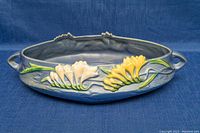 Front view of the round Roseville pottery bowl with two handles and yellow and white flower design.