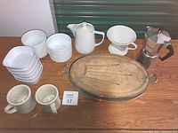 Full set of bowls, ramekins, coffee pots, mugs, and silver serving dish with wooden insert on wooden table.
