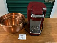 Photo showing the red Keurig coffee maker and three nested copper tone mixing bowls on a wooden surface.