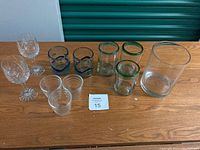 Photo showing 11 glass items: 2 lead crystal stemware glasses, 3 small juice glasses, 2 small decorative glasses (blue and green), 3 medium glasses with colored rims (two green, one blue), and a glass vase.