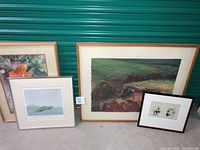 Four framed watercolor artworks placed on the floor against a green door, showing relative sizes and framing styles.
