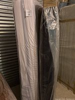 Full-size white mattress and matching box spring wrapped in plastic standing upright in storage unit.