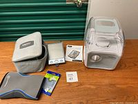 Photo showing Home Medics Therapy automatic blood pressure monitor, carrying case, Pro Care humidifier, Rehband knee brace, and foot insoles on wooden floor.