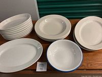 Lot of various porcelain dinnerware and serving pieces including cream/off-white plates, large platters, casserole dishes, and a blue and white bowl.