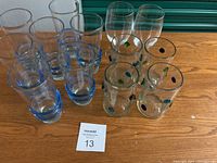 Photo showing the full lot of 13 glasses on wooden surface with auction tag