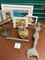 Overview photo of all nautical decor items including reclining mermaid statue, rope doorstop, framed photos and signs, telescope/kaleidoscope on table
