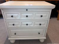 Front angle view of off-white distressed nightstand showing three narrow drawers on top row, one deep drawer below, sturdy solid base with rounded feet.