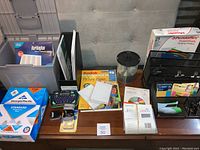 Wide view of office supplies showing paper packs, label maker, blank CDs/DVDs, organizer bins, and assorted labels.
