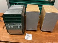 Full view of Panasonic stereo system with two beige cloth covered speakers on wooden table.