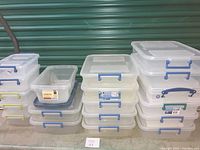Wide view of three stacks of plastic storage bins with lids, showing various sizes and colors of locking handles.