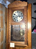 Rectangular oak wall clock showing full front including glass panel and carved floral motif at top.