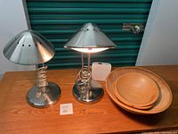 Two silver adjustable height desk lamps alongside three wooden nested bowls on a wooden surface, showing overall condition and size comparison.