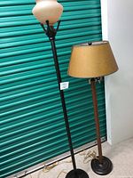 Two floor lamps side-by-side showing the wooden lamp with yellow fabric shade, black base, and four light arms, plus the taller black metal lamp with beige glass shade.