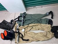 Photo showing two pairs of full length men's fishing waders, one tan and one green, each with feet attached, laid next to two pairs of rubber boots.