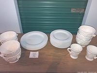 Full lot view on table showing all plates, bowls, and mugs. White and off-white ceramic pieces with different sizes and textures. Lot tag 73 visible.