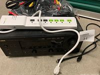 Yamaha HTR5990 receiver powering up with front panel visible, power strip placed on top.