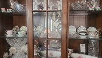 Display of antique cut glass bowls and assorted teacups and saucers in cabinet.
