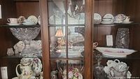 Overall view of cabinet containing Baccarat crystal pieces and antique German porcelain dishes with floral designs.