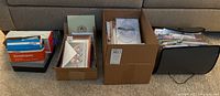 Four boxes lined up on the floor containing greeting cards and envelopes, some in plastic wrap.