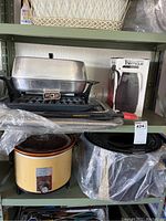 Two shelves with kitchen items including crock pot, electric skillet, baking pans, and Thermos carafe