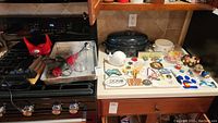Overview of countertop area and stove showing collection of kitchen items including magnets, snowglobes, roasting pan, baking pan, and utensil