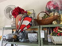 Shelf displaying patriotic hanging hot air balloon, silver garden bust sculpture, mosaic vase, small fan, and a basket with faux flowers.