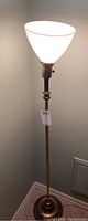 Full view of the first floor lamp showing milk glass shade atop a brass vertical column and base, lit to demonstrate light quality.