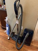 Full view of Kenmore Whispertone vacuum with metal wand, hose, floor nozzle, and cleaning tool in packaging next to it on floor.
