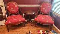 Pair of matching La-Z-Boy armchairs with wooden frames and red floral upholstery, situated side by side with small round table between them on hardwood floor.