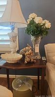 Overview of table showing Lenox bowl, table lamp, elephant figurines, vase with faux white roses, and green hat box with ribbon.