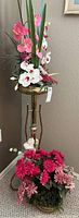 Full view of brass plant stand with faux flower arrangement on top and additional faux flowers at base