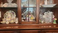 Wide view of the wooden cabinet shelf displaying the Nippon tea set, crystal decanter, Staffordshire and Adderley figurines, and glassware.
