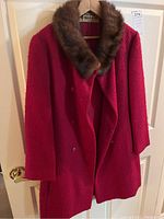 Full front view of red fur coat with brown mink fur collar, hanging on a door