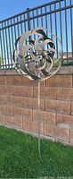 Large spiral wind spinner yard art stake placed in grass in front of stone wall
