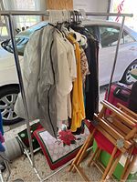 Metal garment rack with clothes hanging and car in background.