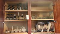 Cabinet shelf with smoked glass stemware, clear glass salt & pepper shakers, covered butter dishes, and small glass plates and bowls.