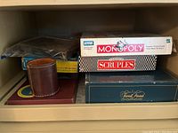 Stacked vintage board game boxes including Monopoly, Scruples, Trivial Pursuit, and a leather dice cup.