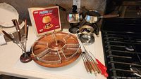 Wide view showing vintage fondue set assembled with lazy susan, six scalloped glass dishes arranged in wooden base, and fondue forks on wooden stand.
