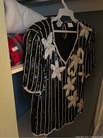 Black dress with detailed floral and stripe bead and sequin embroidery on hanger in closet