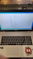 Asus laptop with screen on showing system information and factory reset status, silver keyboard, and partial view of black keyboard above it.