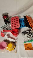 Photo showing various silicone mould trays, measuring cups and spoons, metal cookie cutters, silicone baking cups, and packaged tea infuser.