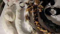 Five pairs of assorted furry white, black, tiger-striped, and leopard-spotted ears and tails laid out on a surface.