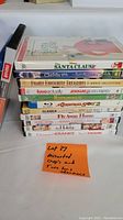 Photo showing a stack of 11 assorted DVDs with titles visible and two lens cleaners placed beside them.